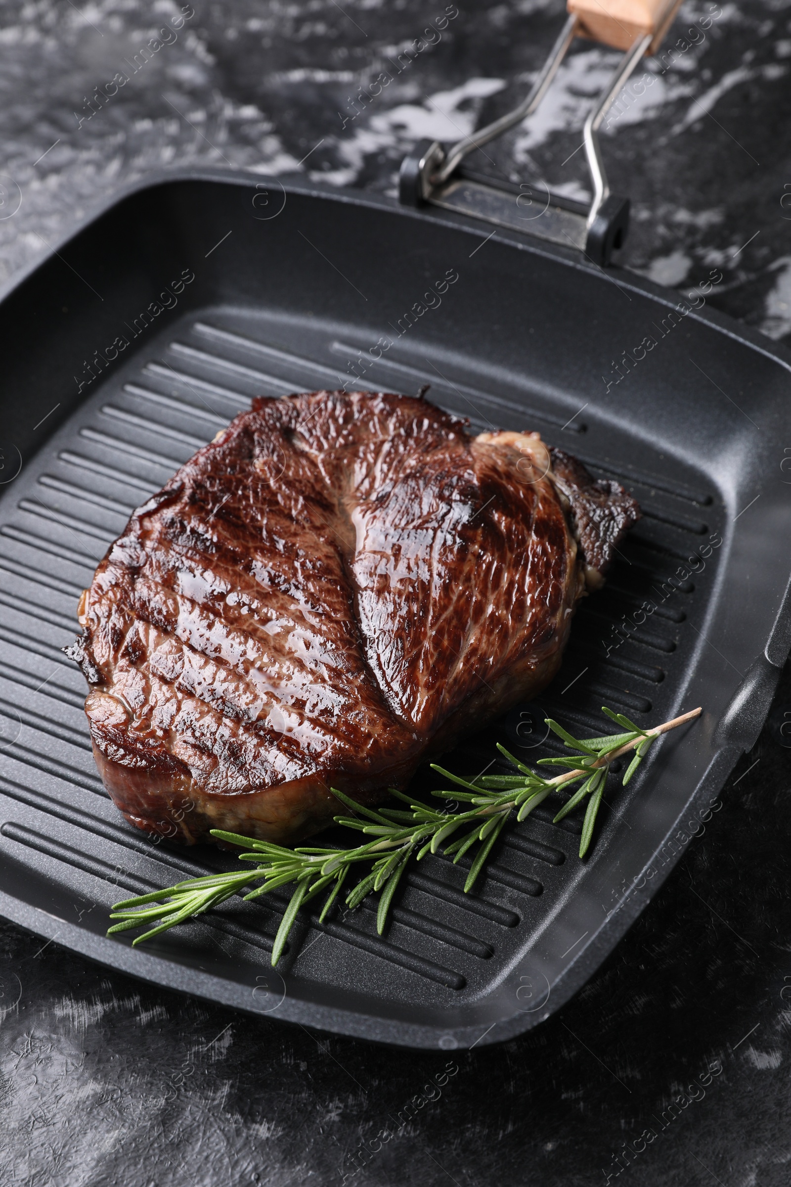 Photo of Grill pan with delicious fried beef meat and rosemary on grey textured table