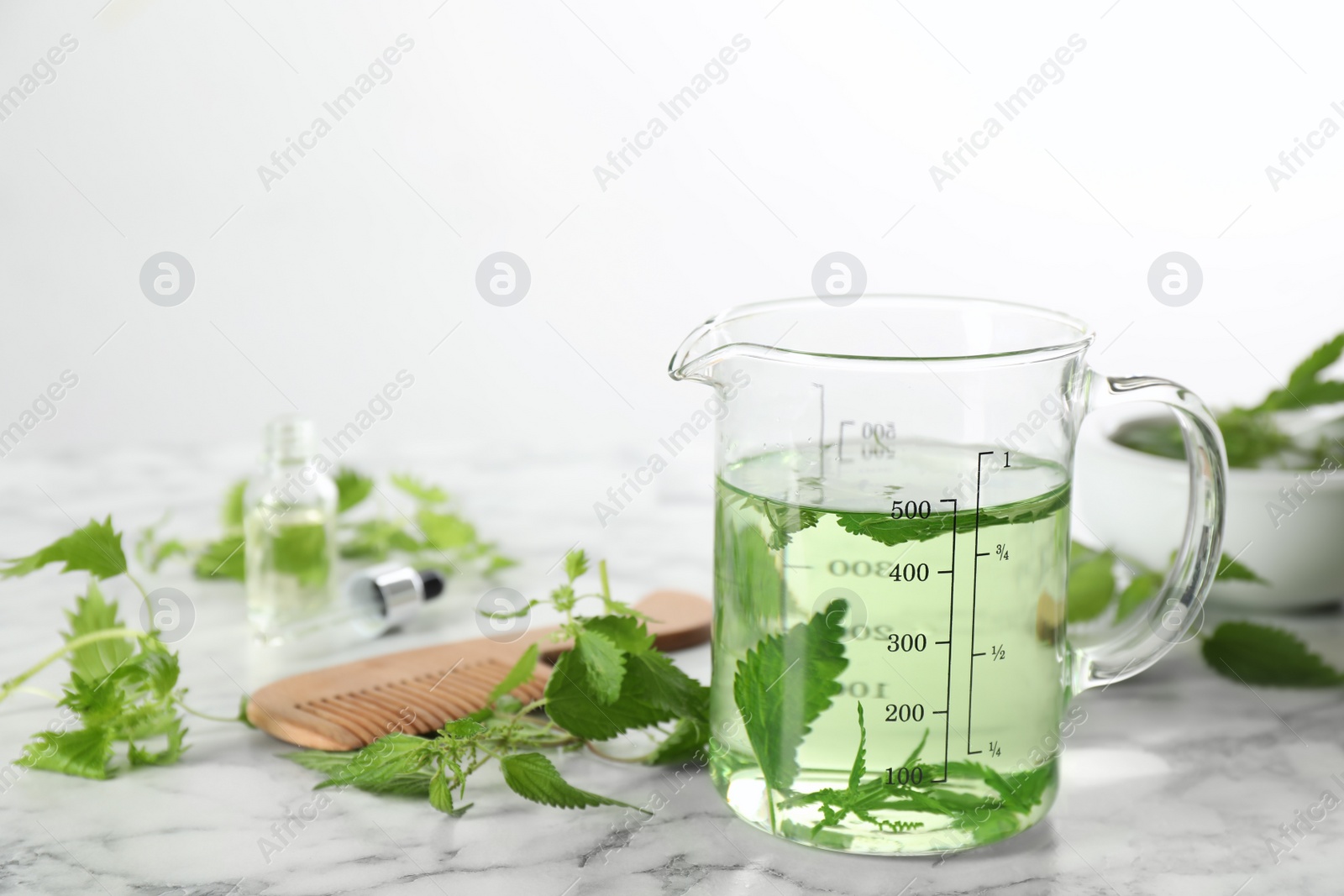 Photo of Stinging nettle, extract and comb on white marble background. Natural hair care