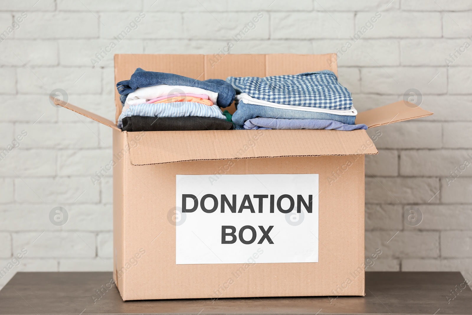 Photo of Donation box with clothes on table against brick wall