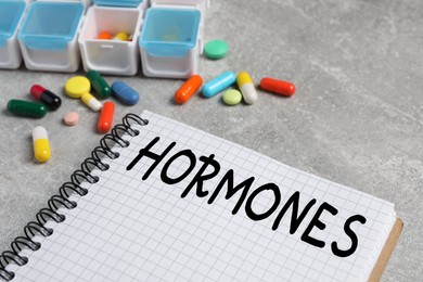 Photo of Notebook with word HORMONES and pills on grey table, closeup