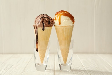 Different ice cream with toppings in wafer cones served on white wooden table