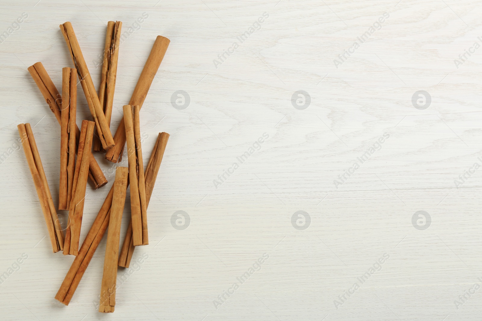 Photo of Aromatic cinnamon sticks on white wooden table, flat lay. Space for text