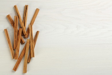 Aromatic cinnamon sticks on white wooden table, flat lay. Space for text