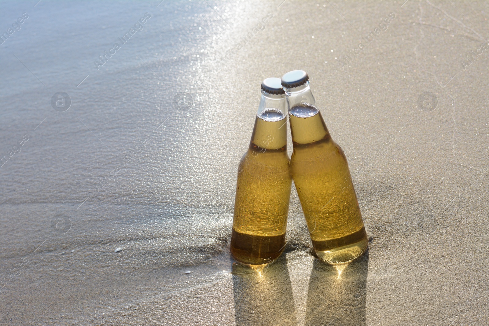 Photo of Bottles of cold beer on sandy beach, space for text