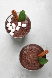 Photo of Cups of delicious hot chocolate with marshmallows, cinnamon stick and mint on light grey table, flat lay