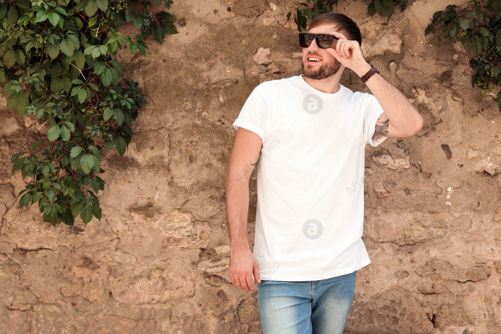 Photo of Young man wearing white t-shirt near stone wall on street