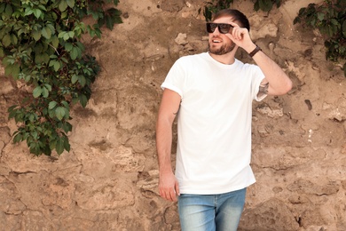 Young man wearing white t-shirt near stone wall on street