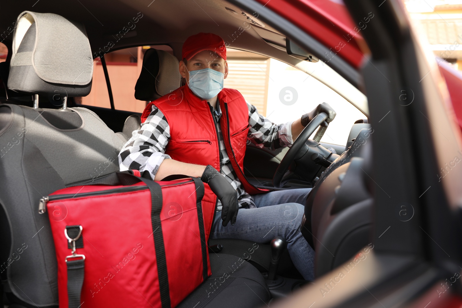 Photo of Courier in protective mask and gloves with thermobag inside car. Food delivery service during coronavirus quarantine
