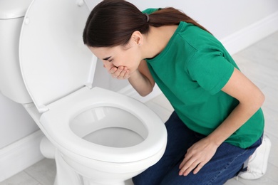 Photo of Young woman suffering from nausea over toilet bowl indoors