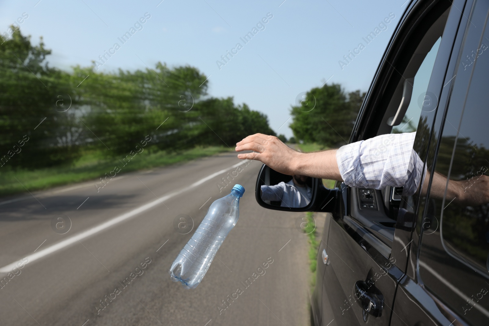 Photo of Driver throwing away plastic bottle from car window. Garbage on road