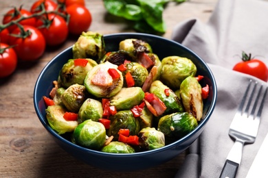 Photo of Delicious Brussels sprouts with bacon in bowl on wooden table