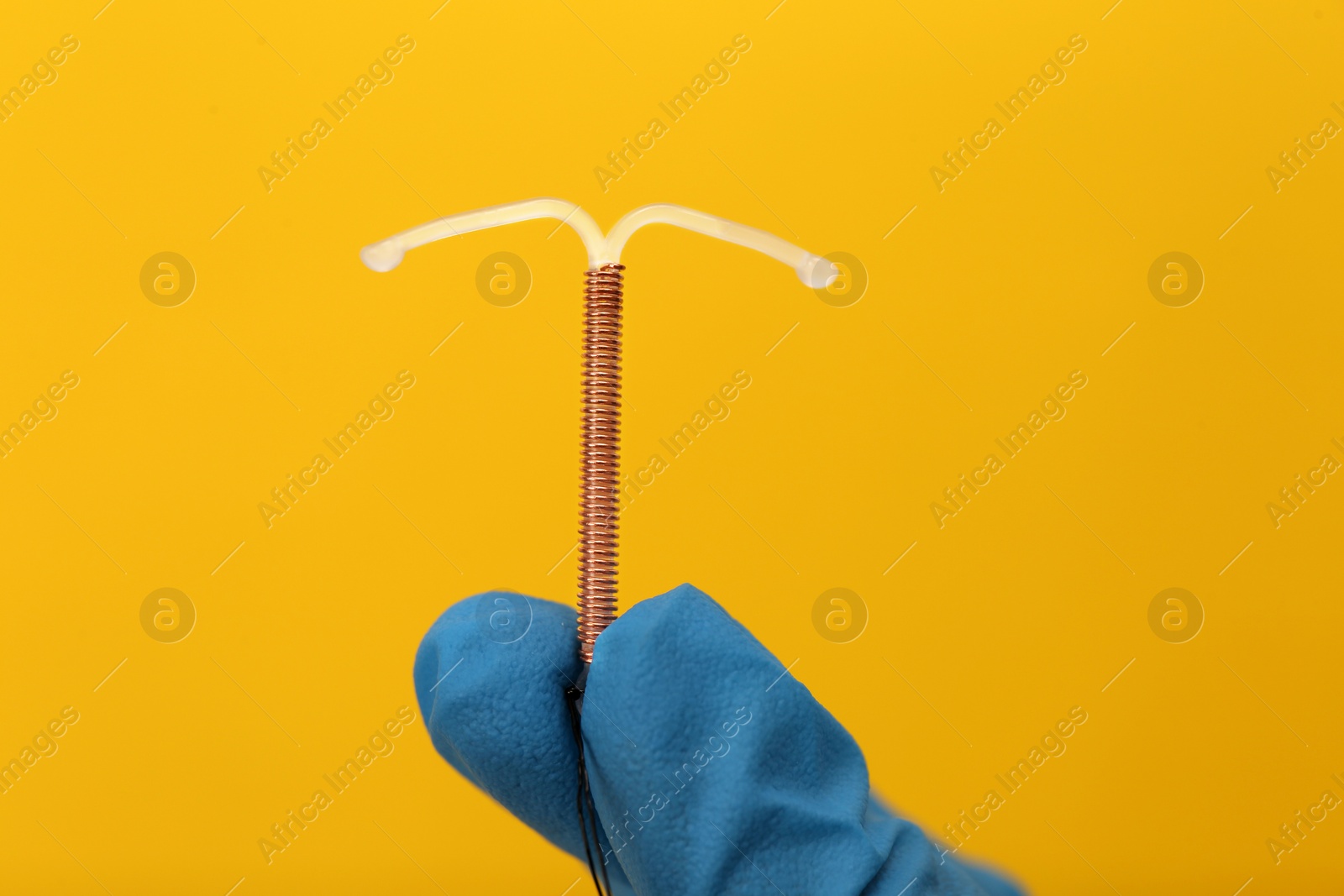 Photo of Doctor holding T-shaped intrauterine birth control device on yellow background, closeup