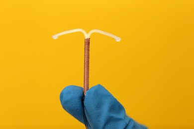 Photo of Doctor holding T-shaped intrauterine birth control device on yellow background, closeup