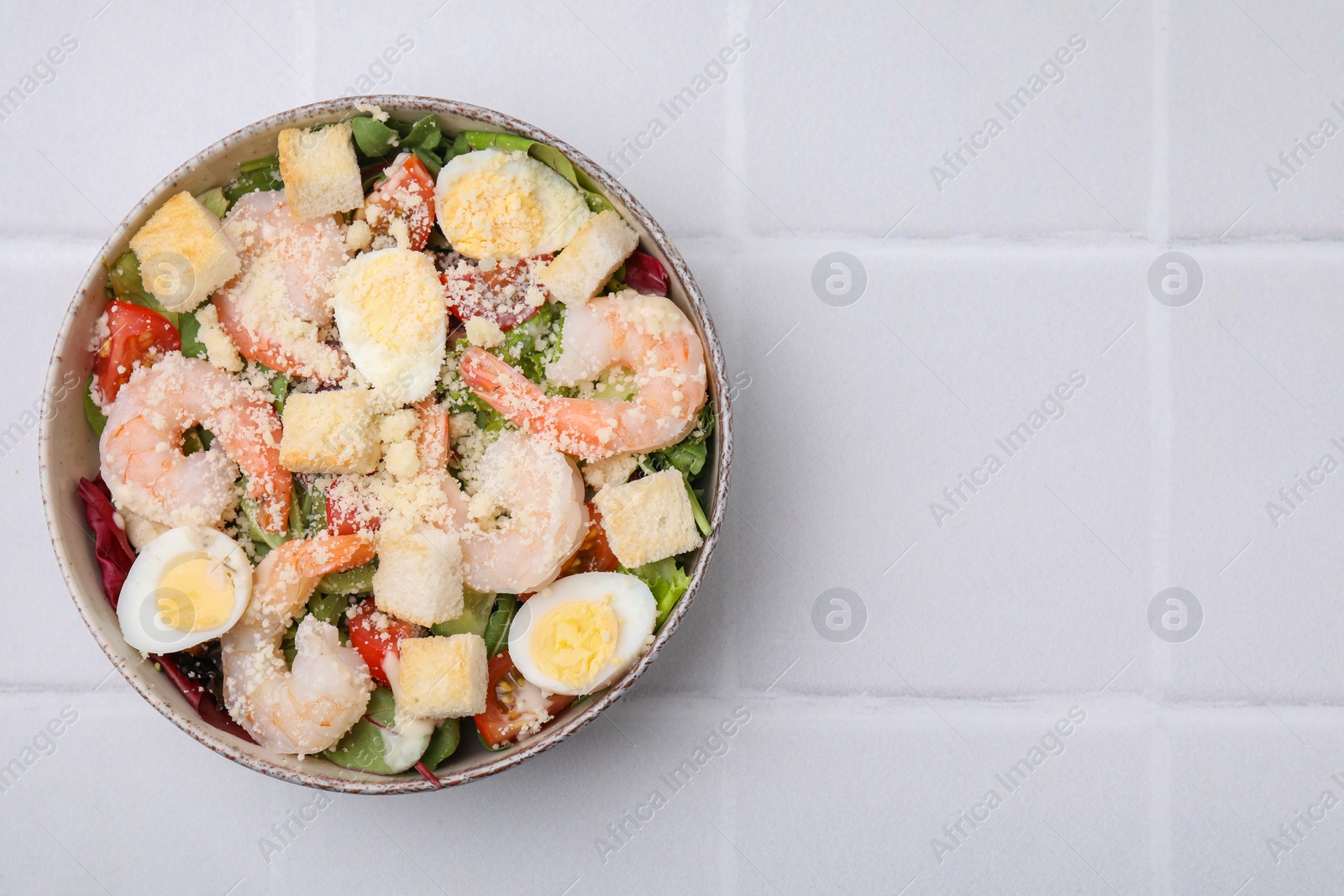 Photo of Delicious Caesar salad with shrimps on white tiled table, top view. Space for text