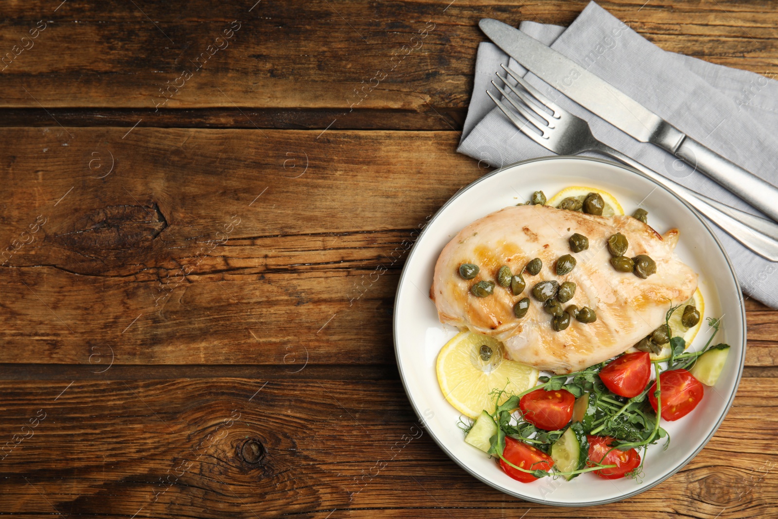 Photo of Delicious cooked chicken fillet with capers and salad served on wooden table, flat lay. Space for text