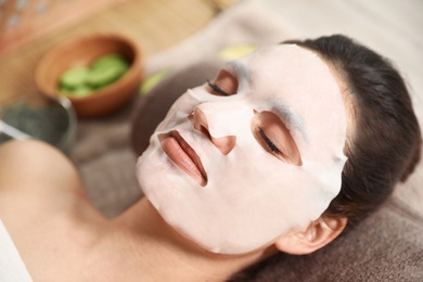 Beautiful woman with cotton mask sheet on face relaxing in spa salon, closeup