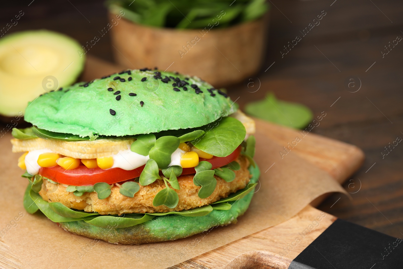 Photo of Tasty green vegan burger with vegetables, patty and microgreens on wooden table, closeup. Space for text