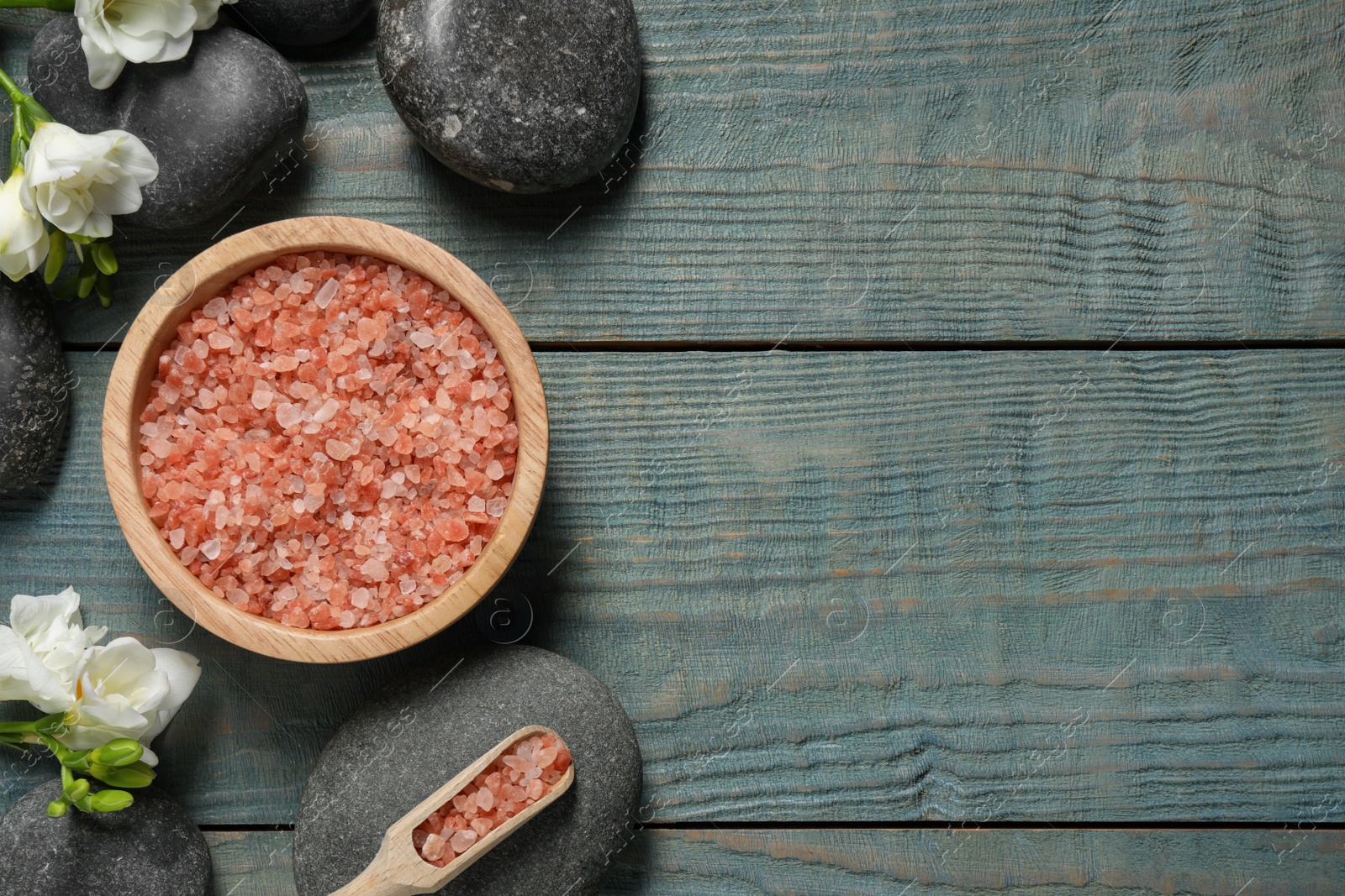 Photo of Sea salt, beautiful flowers and spa stones on blue wooden table, flat lay. Space for text