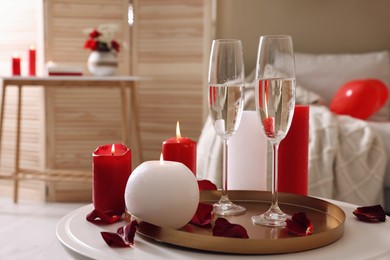 Glasses of sparkling wine, candles and petals on white table indoors. happy Valentine's Day