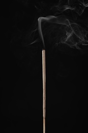 Incense stick smoldering on black background, closeup