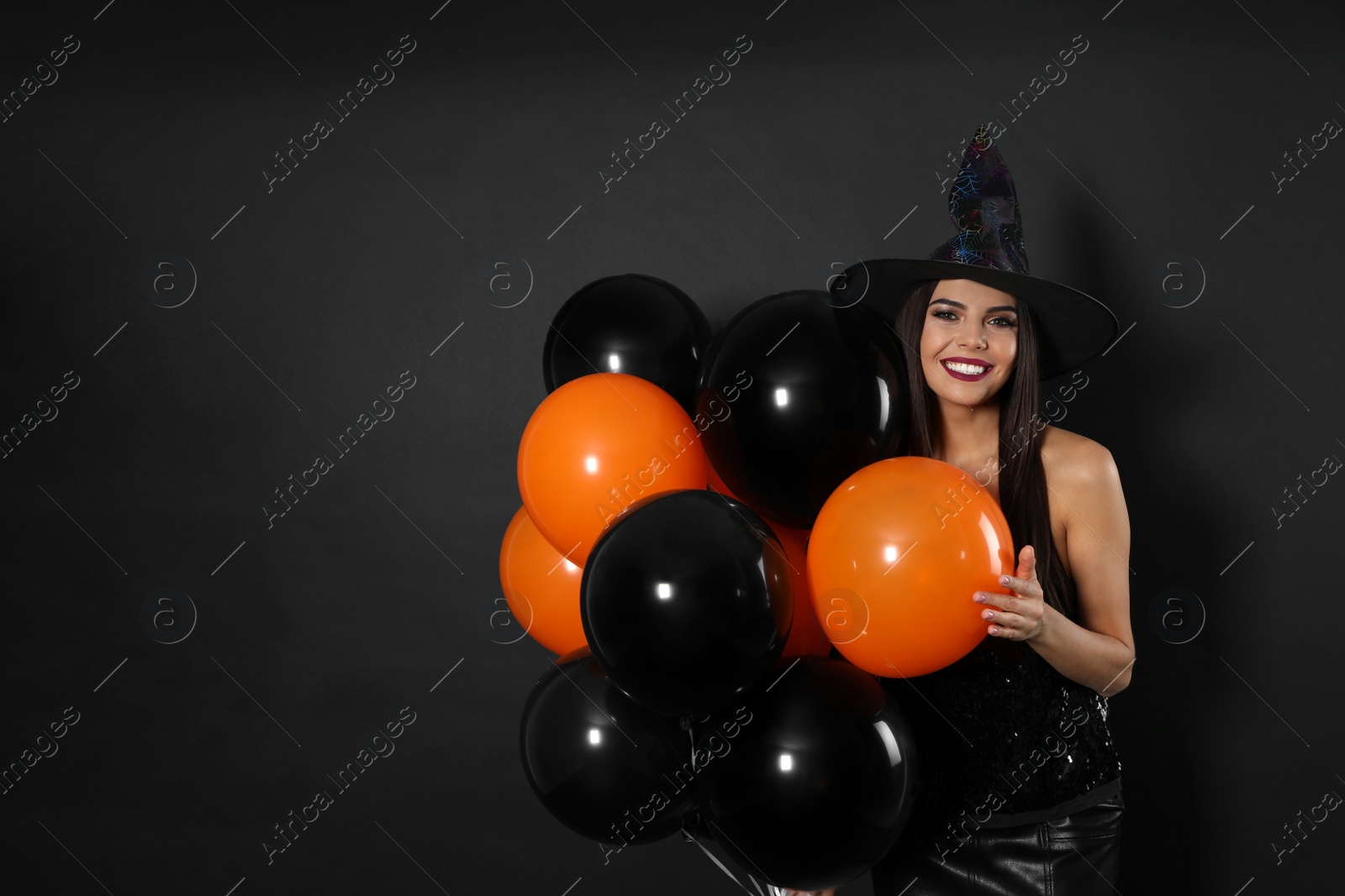 Photo of Beautiful woman wearing witch costume with balloons for Halloween party on black background, space for text