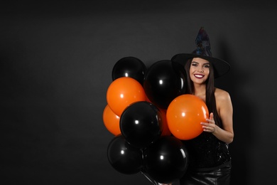 Photo of Beautiful woman wearing witch costume with balloons for Halloween party on black background, space for text