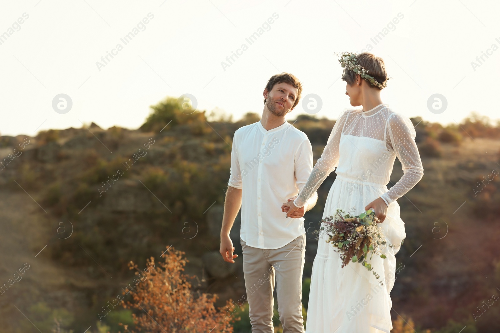 Photo of Happy newlyweds with beautiful field bouquet outdoors