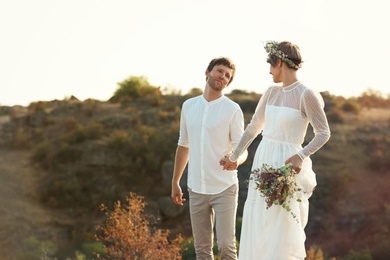 Happy newlyweds with beautiful field bouquet outdoors