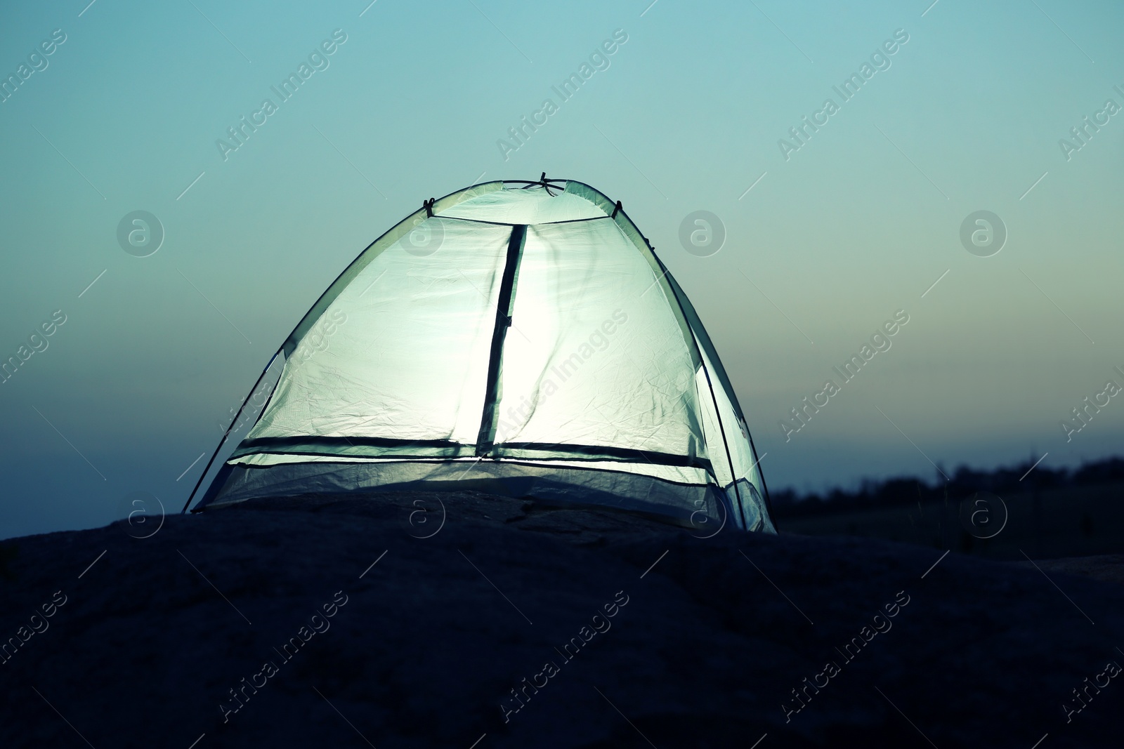 Photo of Small camping tent glowing in twilight outdoors