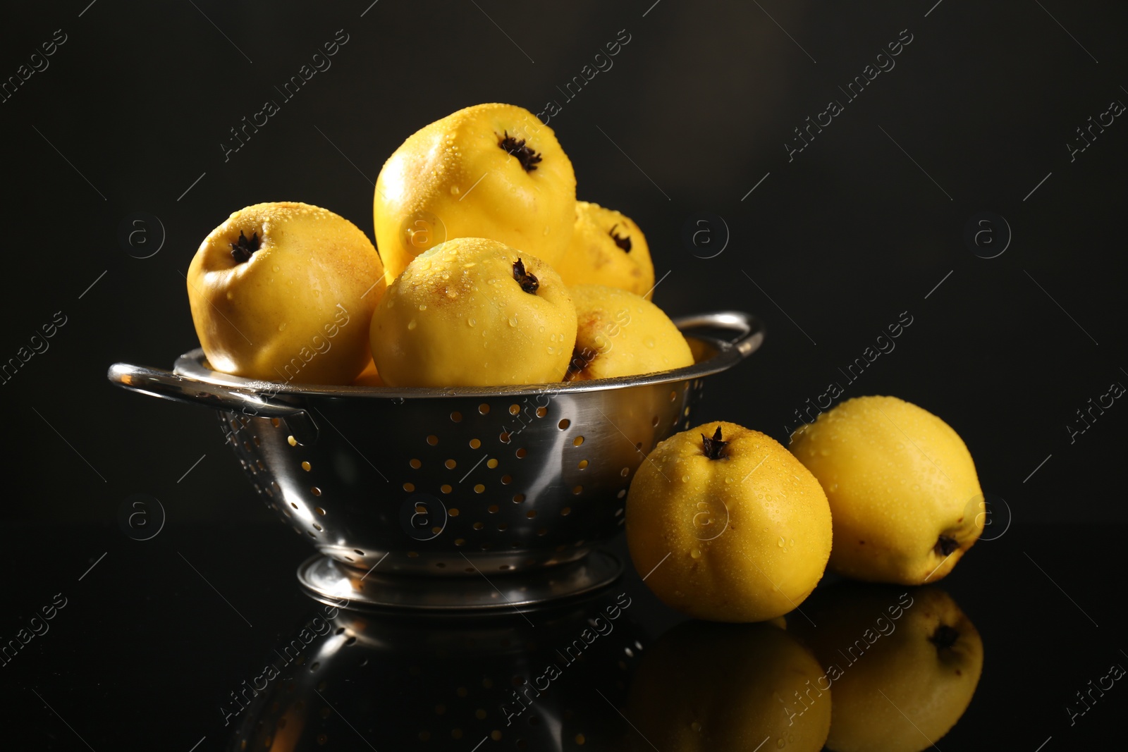 Photo of Tasty ripe quinces and metal colander on black mirror surface