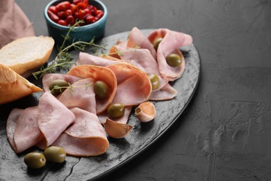 Photo of Tasty ham with olives, garlic and bread on black textured table. Space for text