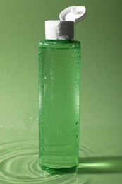 Photo of Wet bottle of micellar water on green background