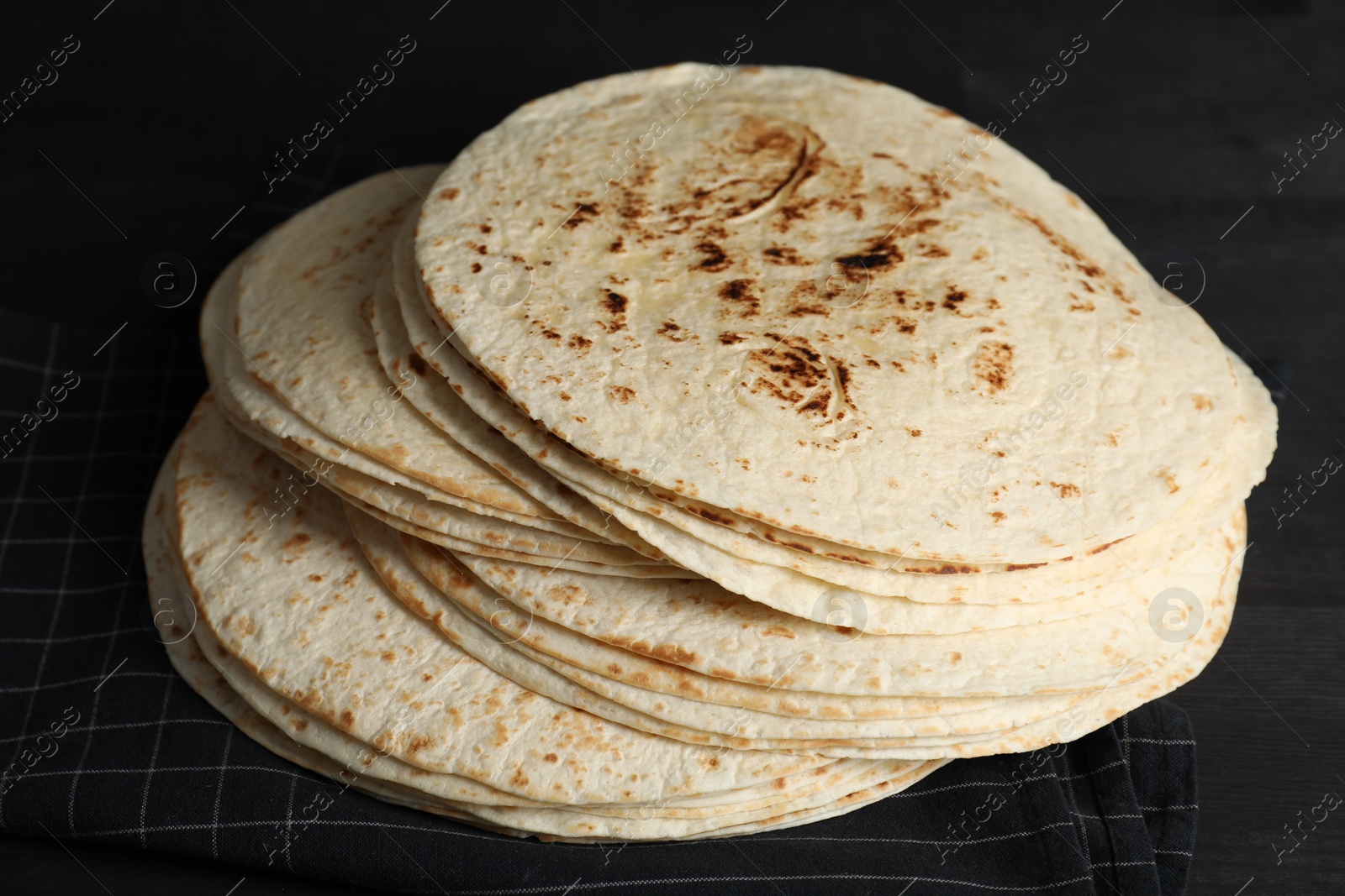 Photo of Many tasty homemade tortillas on black wooden table, closeup