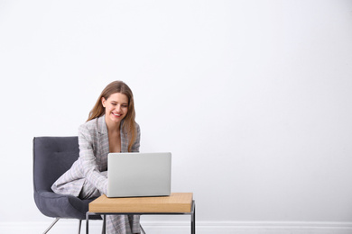 Young woman working with laptop in armchair indoors. Space for text