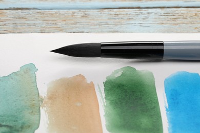 Photo of Sheet of paper with watercolor strokes and brush on light grey wooden table, closeup