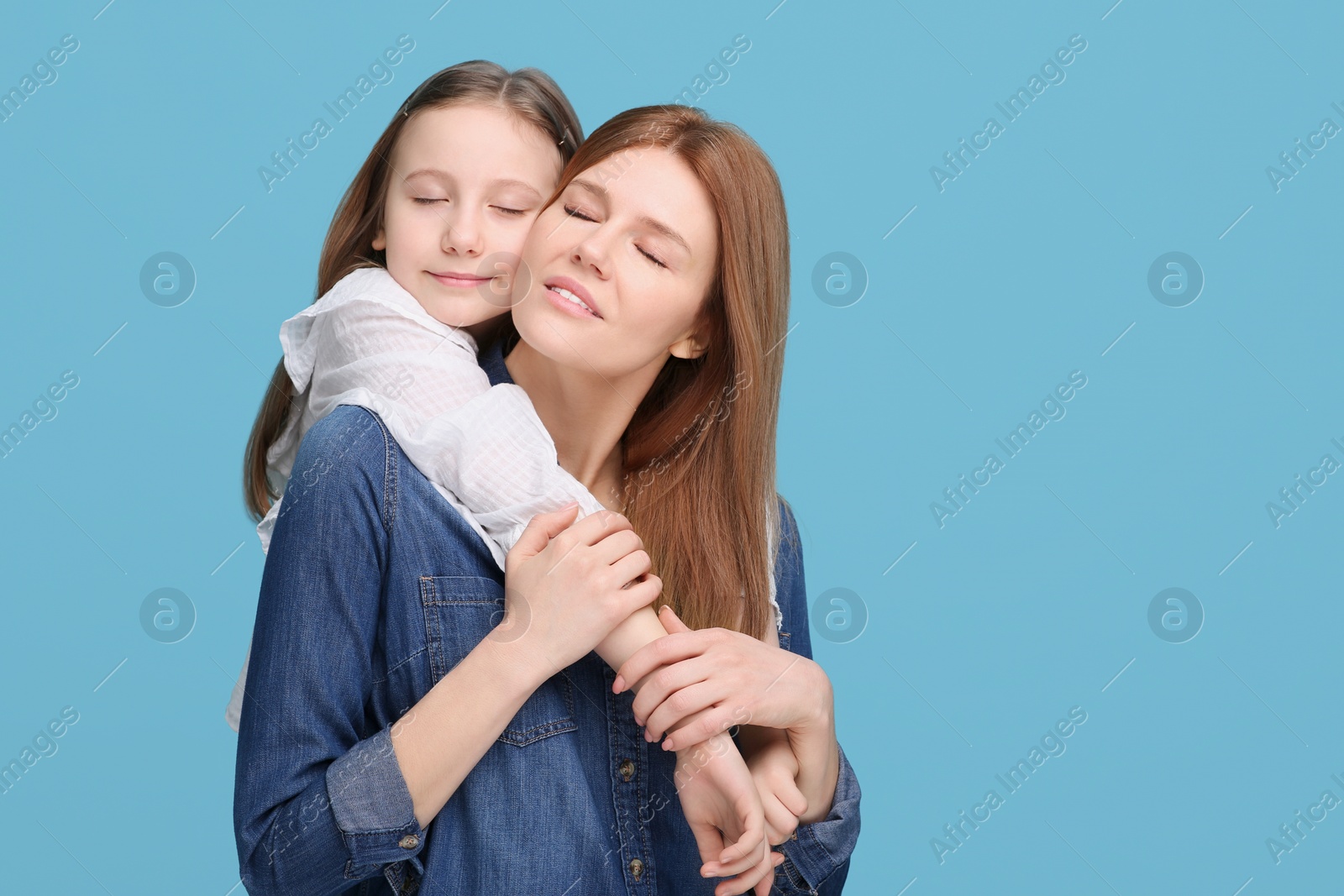 Photo of Portrait of happy mother and her cute daughter on light blue background. Space for text