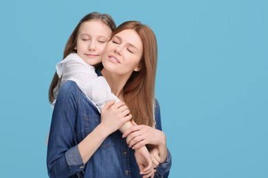 Photo of Portrait of happy mother and her cute daughter on light blue background. Space for text