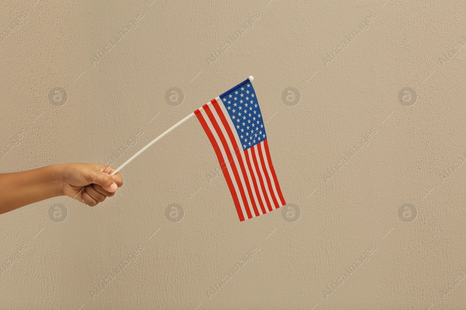 Photo of African-American child holding national flag on beige background, closeup