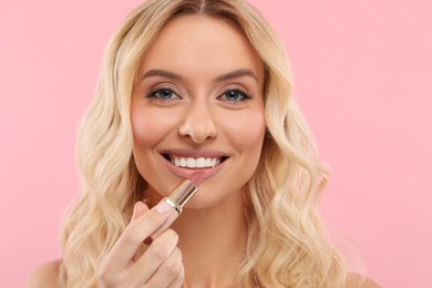 Photo of Beautiful makeup. Smiling woman applying lipstick on pink background, closeup