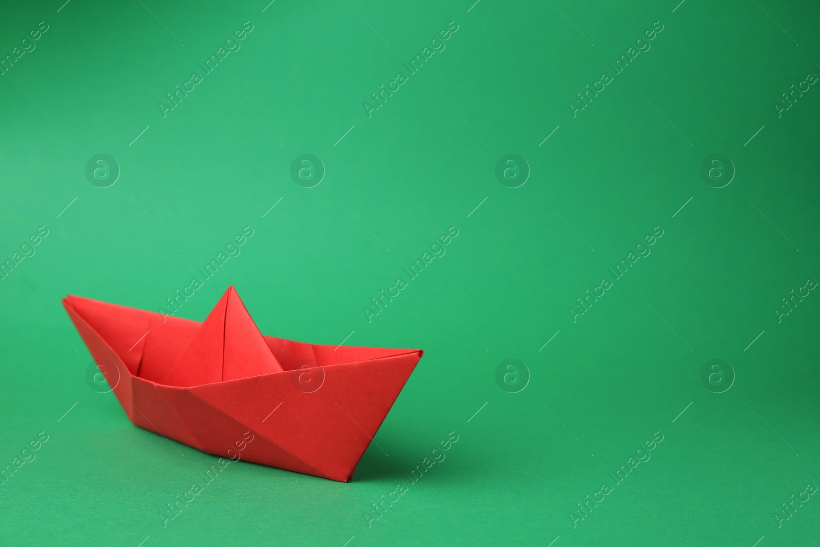 Photo of Origami art. Paper boat on green background, space for text