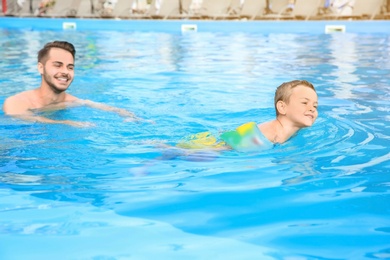 Photo of Father teaching son to swim with inflatable sleeves in pool on sunny day
