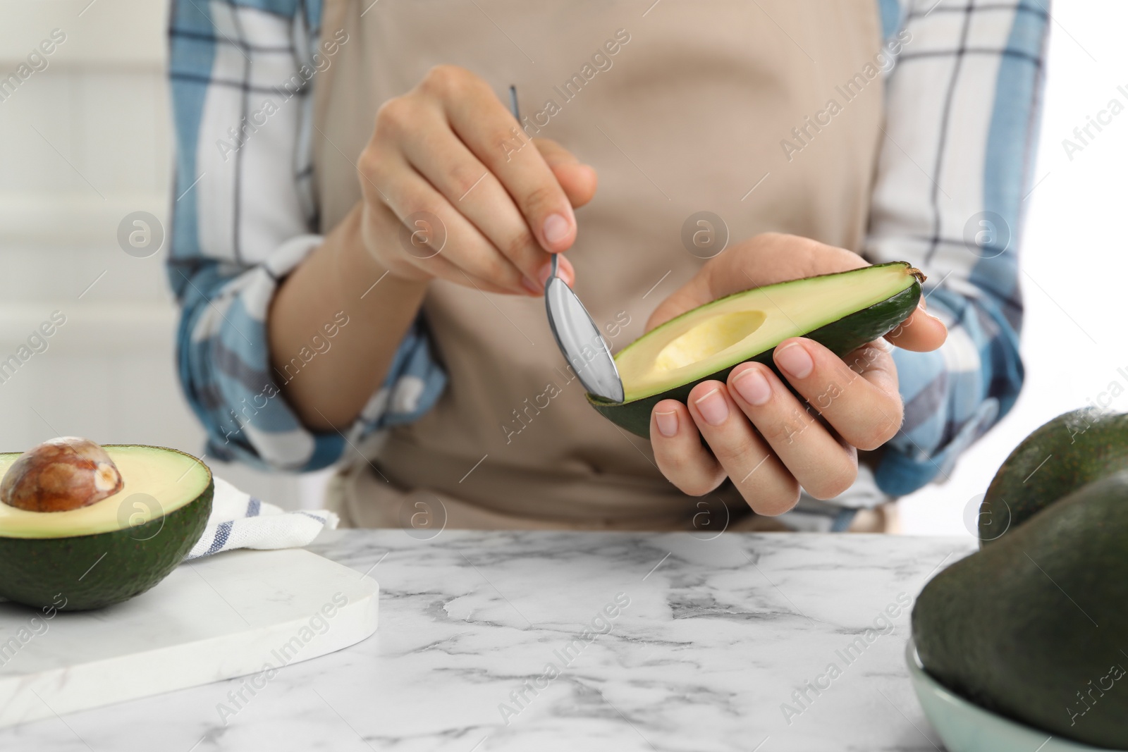 Photo of Woman with half of delicious ripe avocado and spoon at marble table, closeup