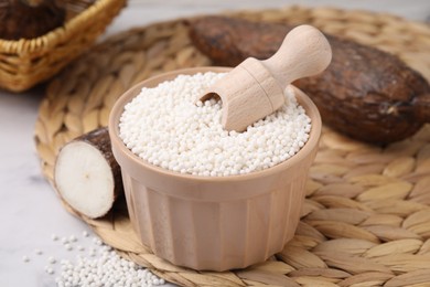 Photo of Tapioca pearls in bowl and cassava roots on wicker mat, closeup