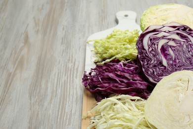 Photo of Different types of cut cabbage on white wooden table, space for text