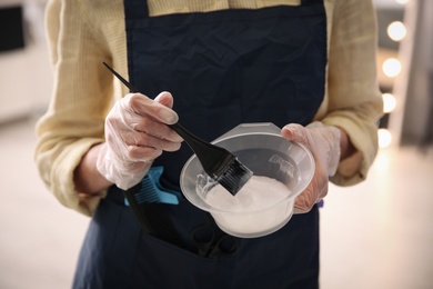 Photo of Professional hairdresser holding bowl with hair dye in beauty salon, closeup