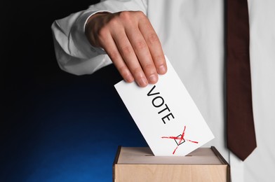 Man putting paper with word Vote and tick into ballot box on dark blue background