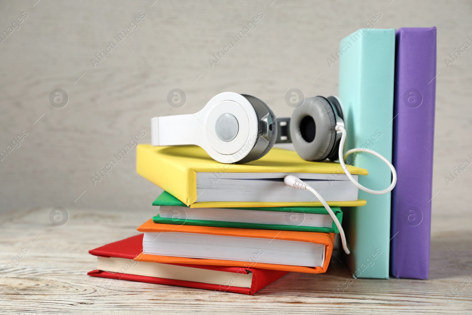 Photo of Modern headphones with hardcover books on wooden table