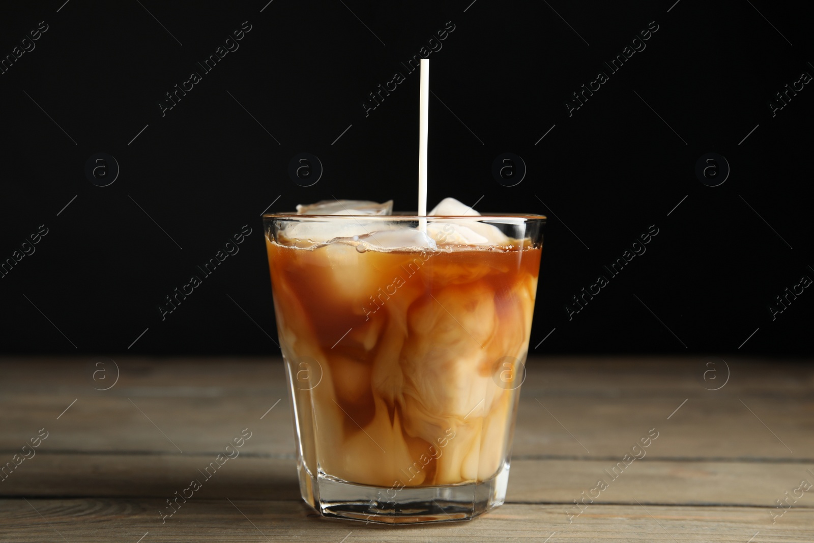 Photo of Pouring milk into glass with coffee on wooden table