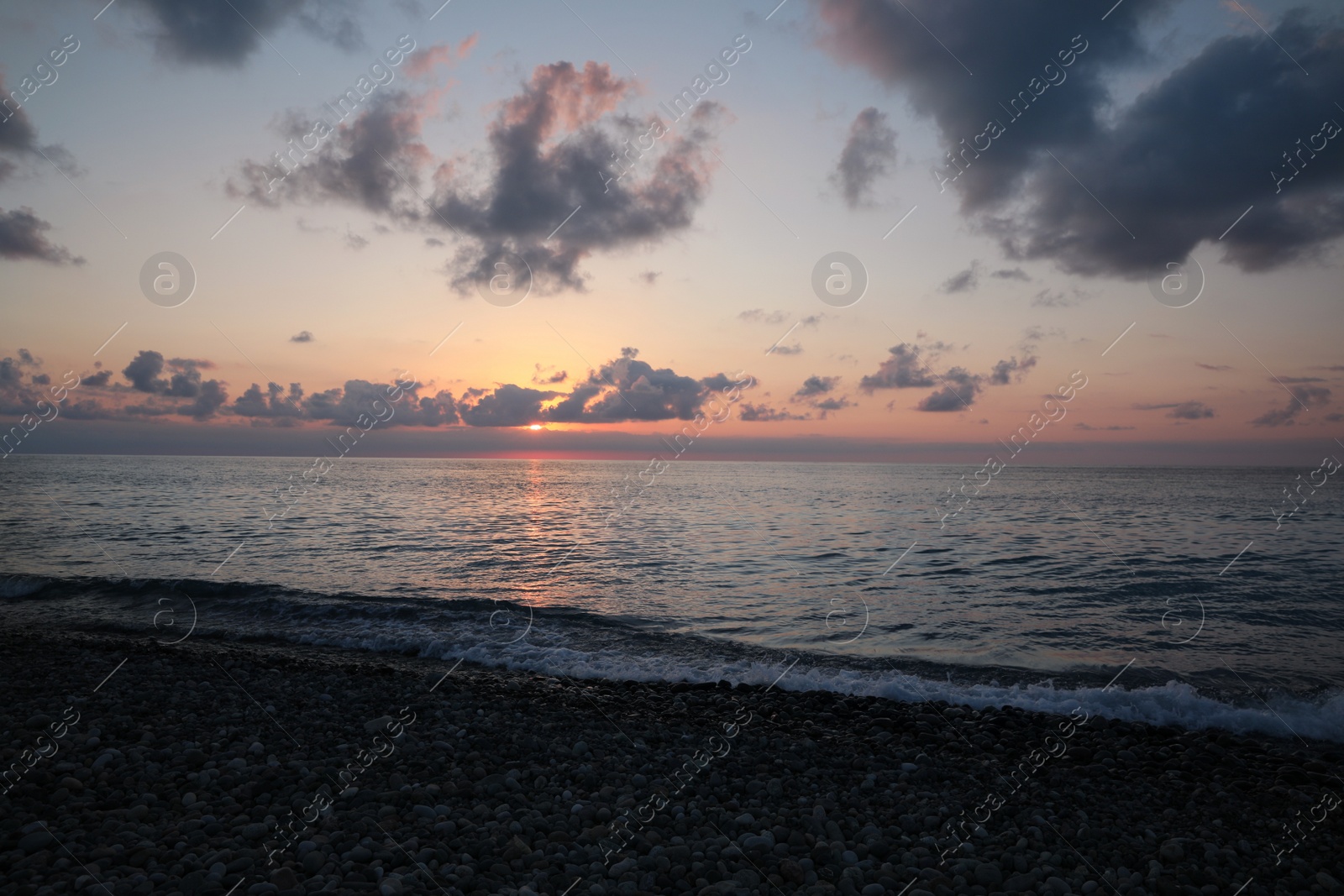 Photo of Picturesque view of pebble beach and sea at sunset