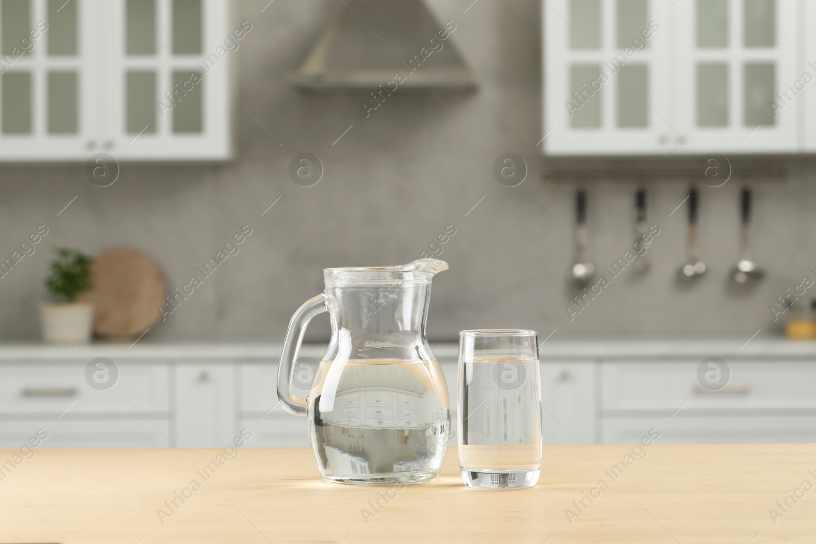 Photo of Glass and jug with water on wooden table in kitchen